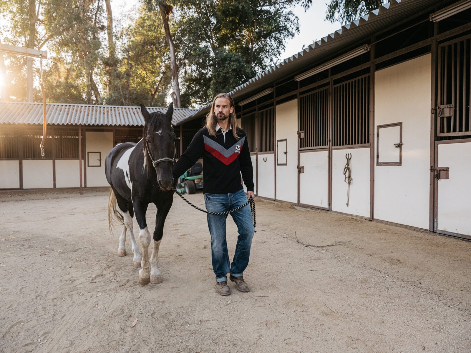 Model walking a black-and-white paint horse past the stables, Shadow Hills Ranch